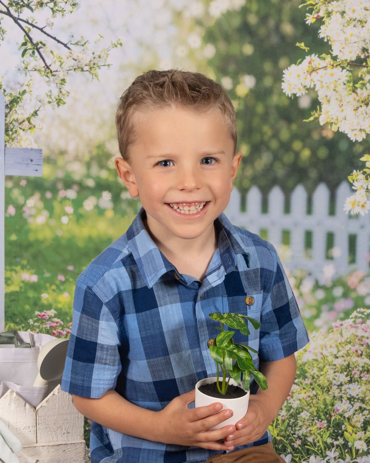 Chase, smiling in a blue plaid shirt and holding a small potted plant